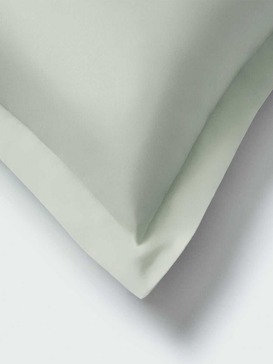 Part of a pillow with aFlorentine Sage-colored pillowcase featuring embroidery along the edge.