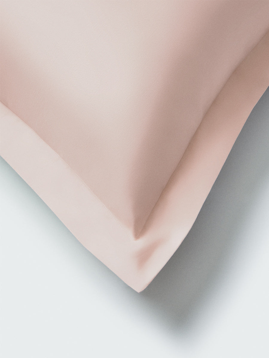 Part of a pillow with a Kyoto Blush-colored pillowcase featuring embroidery along the edge.