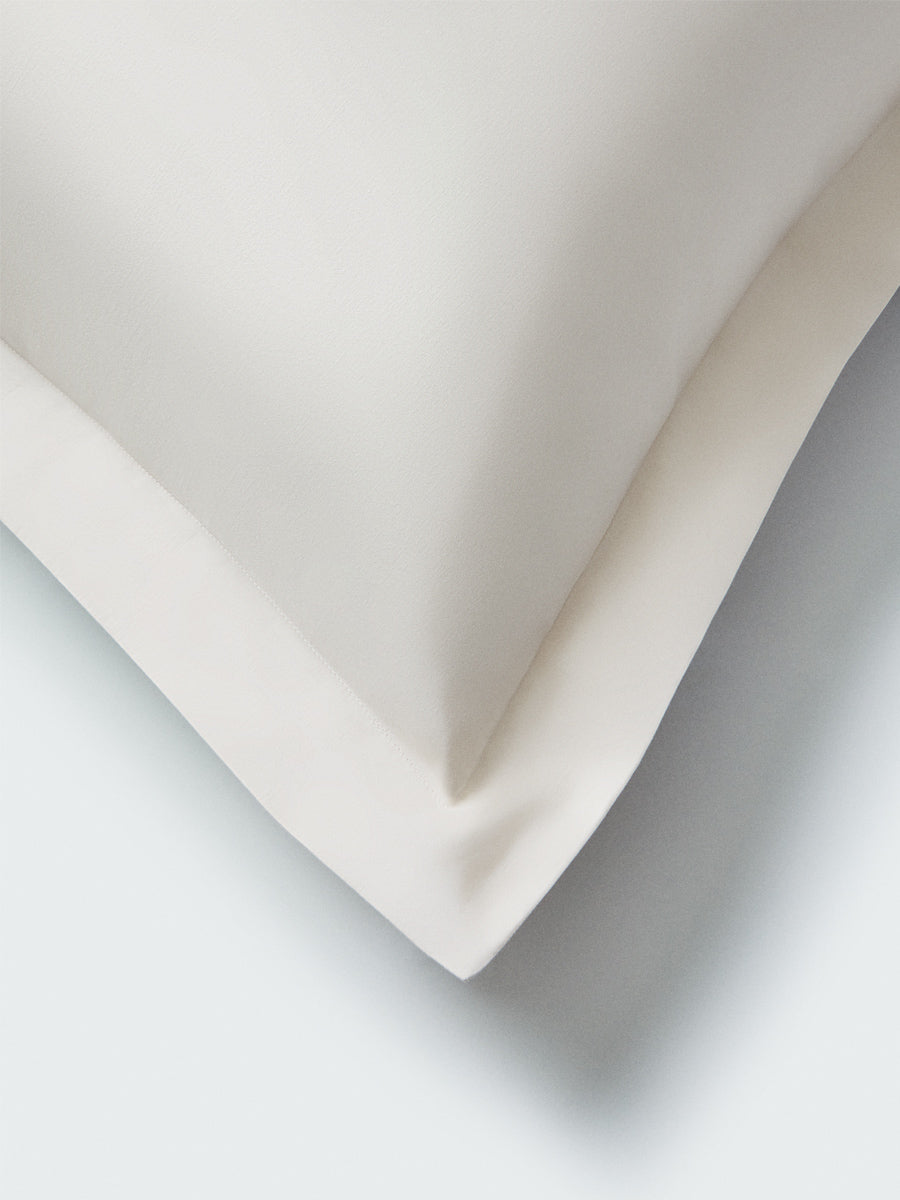 Part of a pillow with a Balinese Pearl colored pillowcase featuring embroidery along the edge.