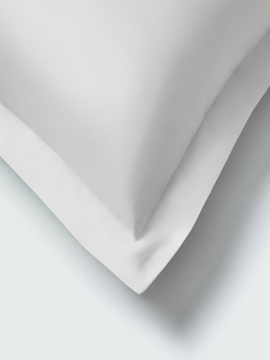 Part of a pillow with a Signature White-color pillowcase featuring embroidery along the edge.