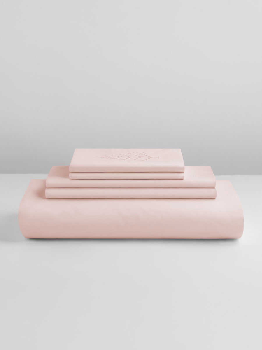 A set of Kyoto Blush-colored sheets, folded into perfect rectangles and stacked on a flat surface.