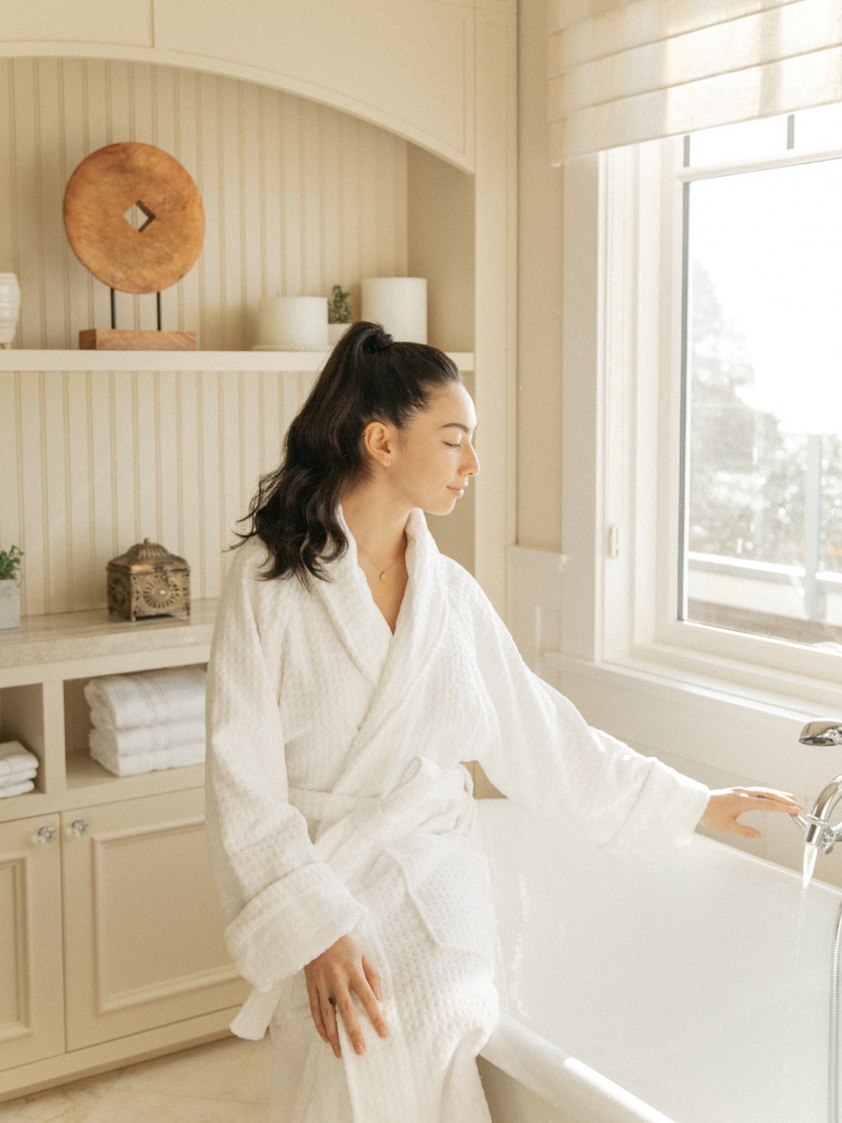 A woman sitting on top of a bathtub, wearing a bathrobe