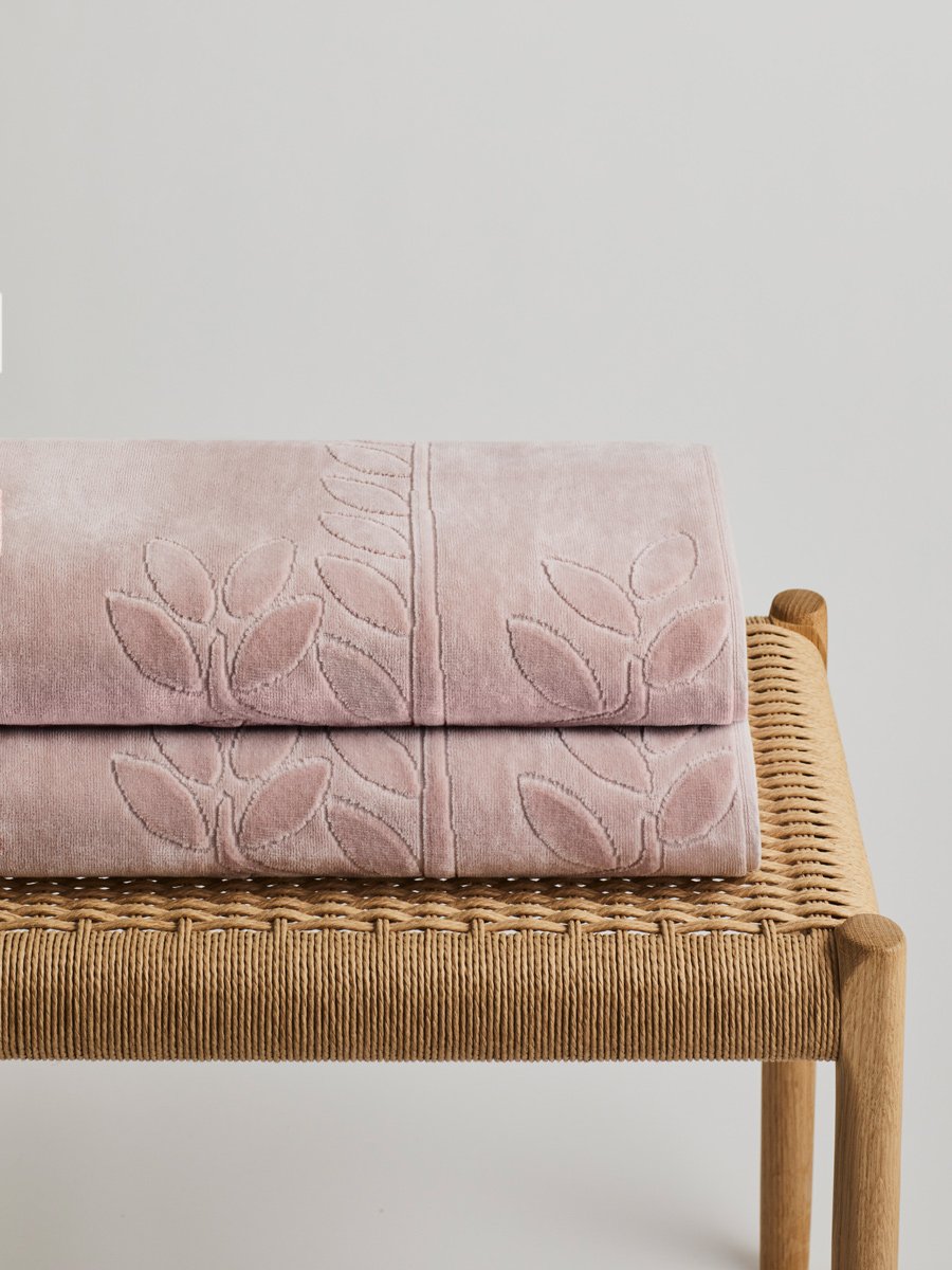 Two 'Hawaiian Sunrise' beach towels folded on a wooden bench. The towels feature a subtle leaf pattern.