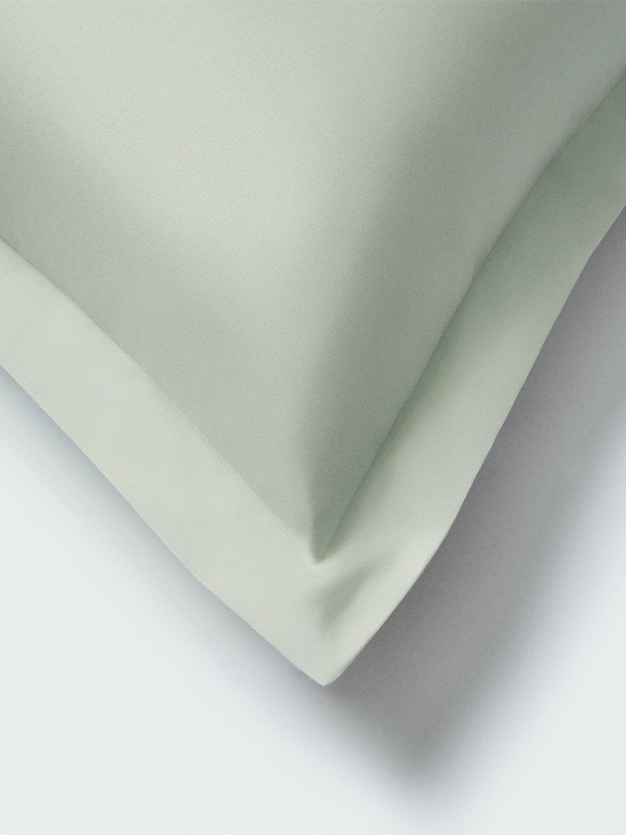 Part of a pillow with a Florentine Sage color pillowcase featuring embroidery along the edge.