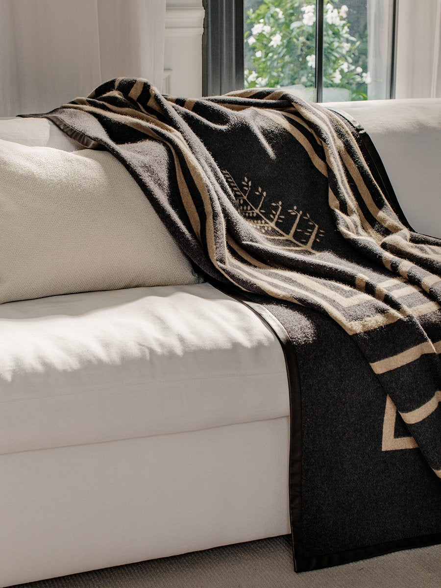 A black throw with a leather trim draped over a white sofa in a living room.