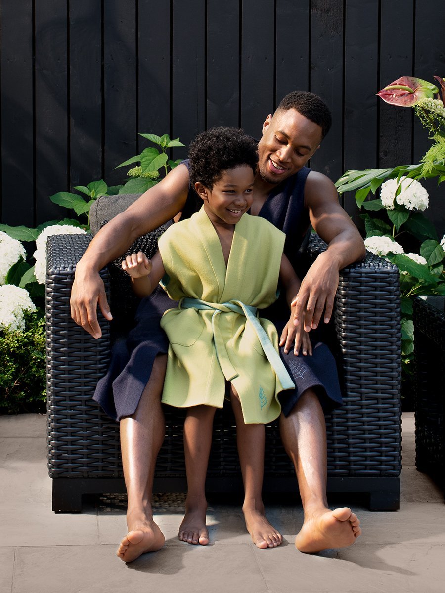 Two figures, a man and a child, relaxing while seated, both dressed in Resort robes.
