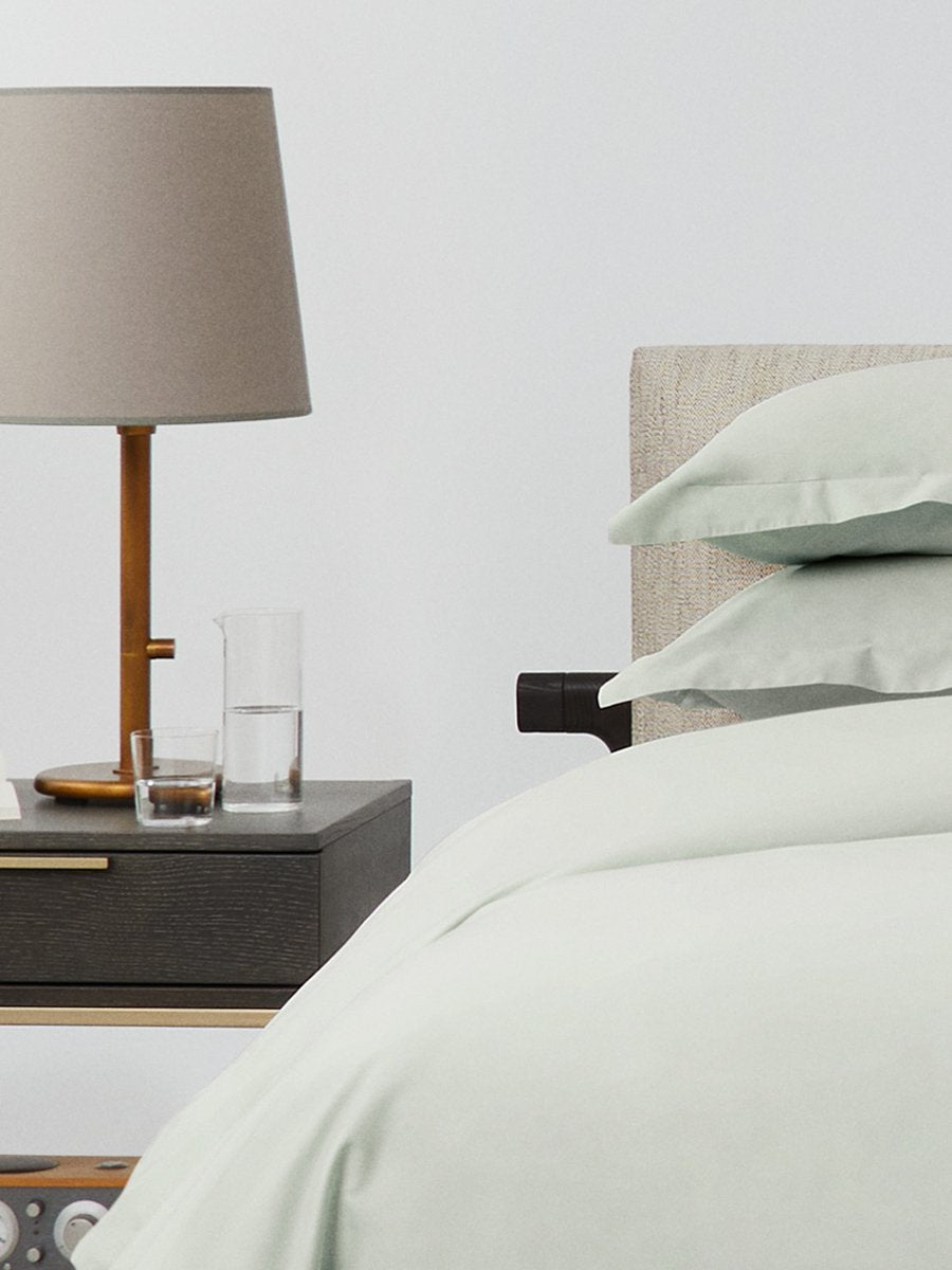 Bed dressed with a duvet in Florentine Sage color and two pillows with embroidery along the edge.