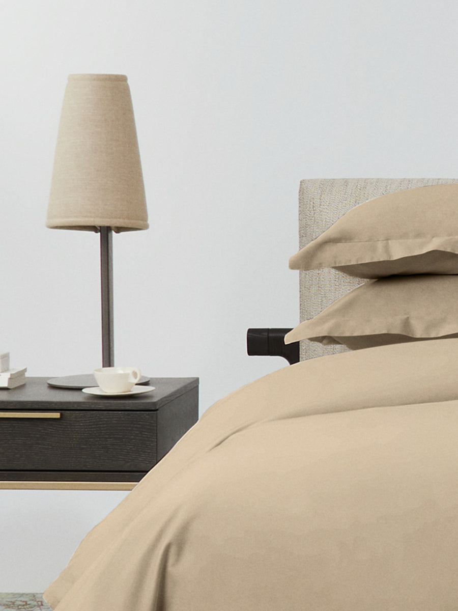 Bed dressed with a duvet in Egyptian Camel color and two pillows with embroidery along the edge.