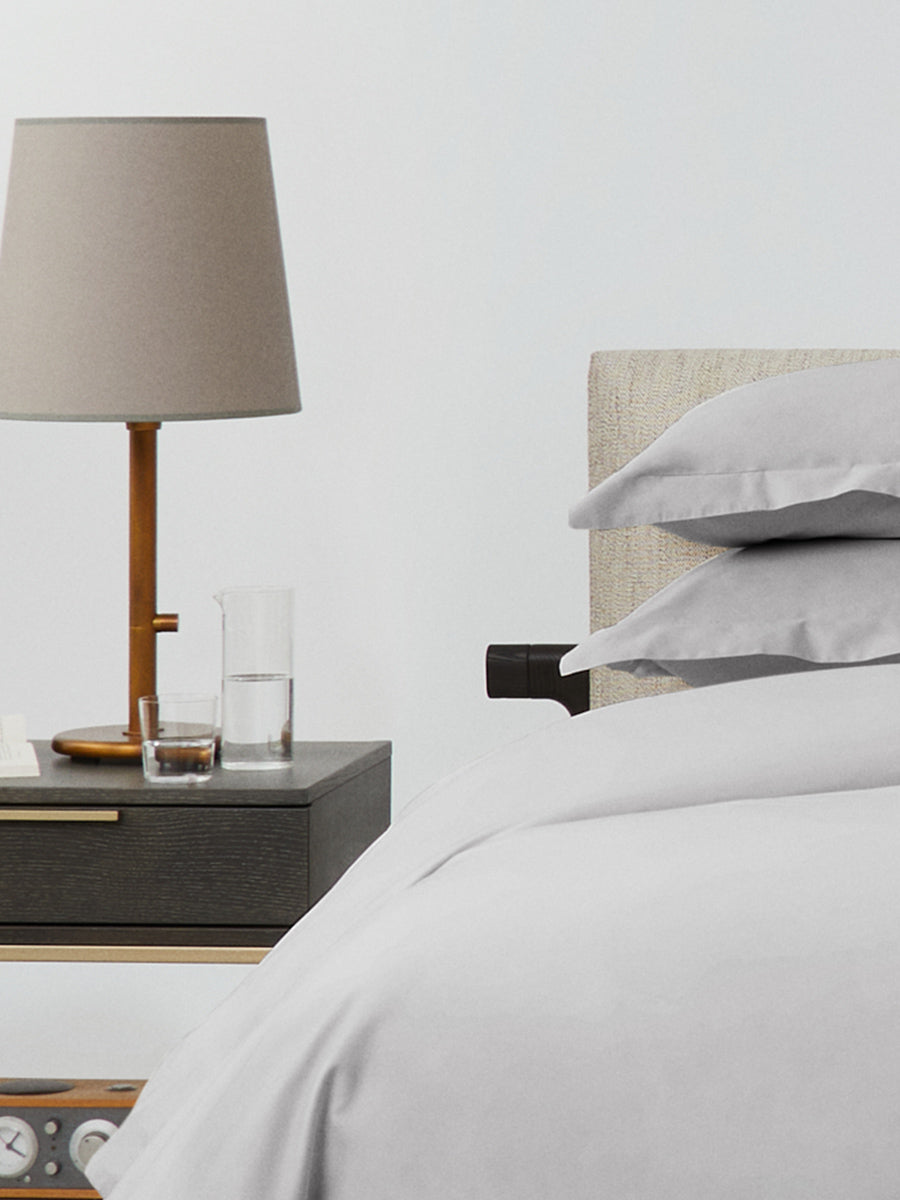 Bed dressed with a duvet in Turkish Silver color and two pillows with embroidery along the edge.
