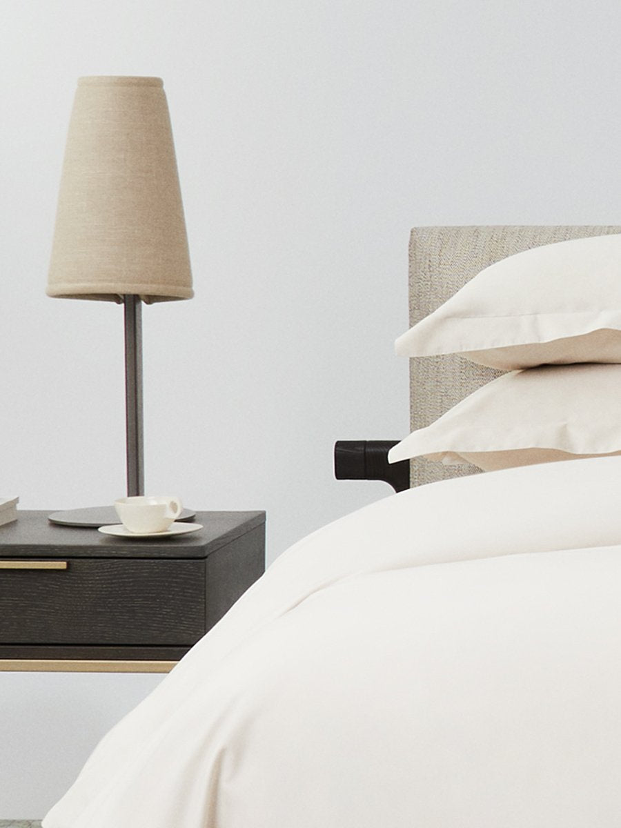 Bed dressed with a duvet in Balinese Pearl color and two pillows with embroidery along the edge.