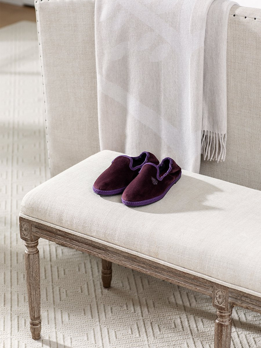 Four Seasons Velvet Slippers in Napa Cabernet placed on a bench in a cozy living room setting