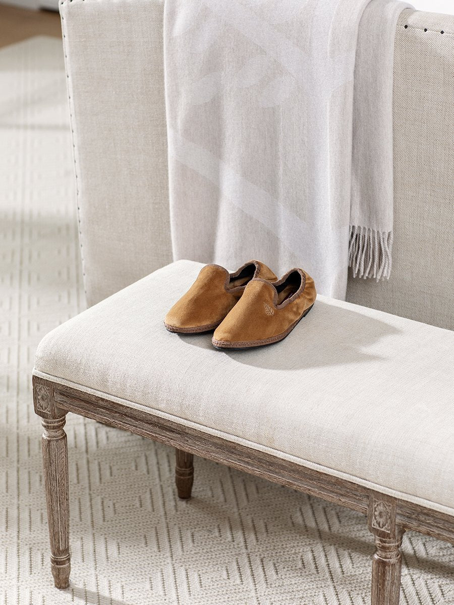 Four Seasons Velvet Slippers in Egyptian Camel placed on a bench in a cozy living room setting