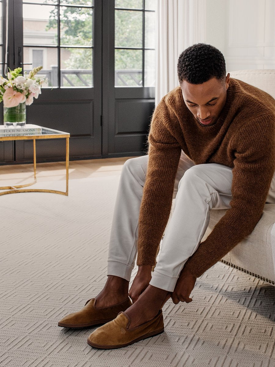 A man putting on the Four Seasons Velvet Slippers in Hampshire Charcoal while sitting on a chair.
