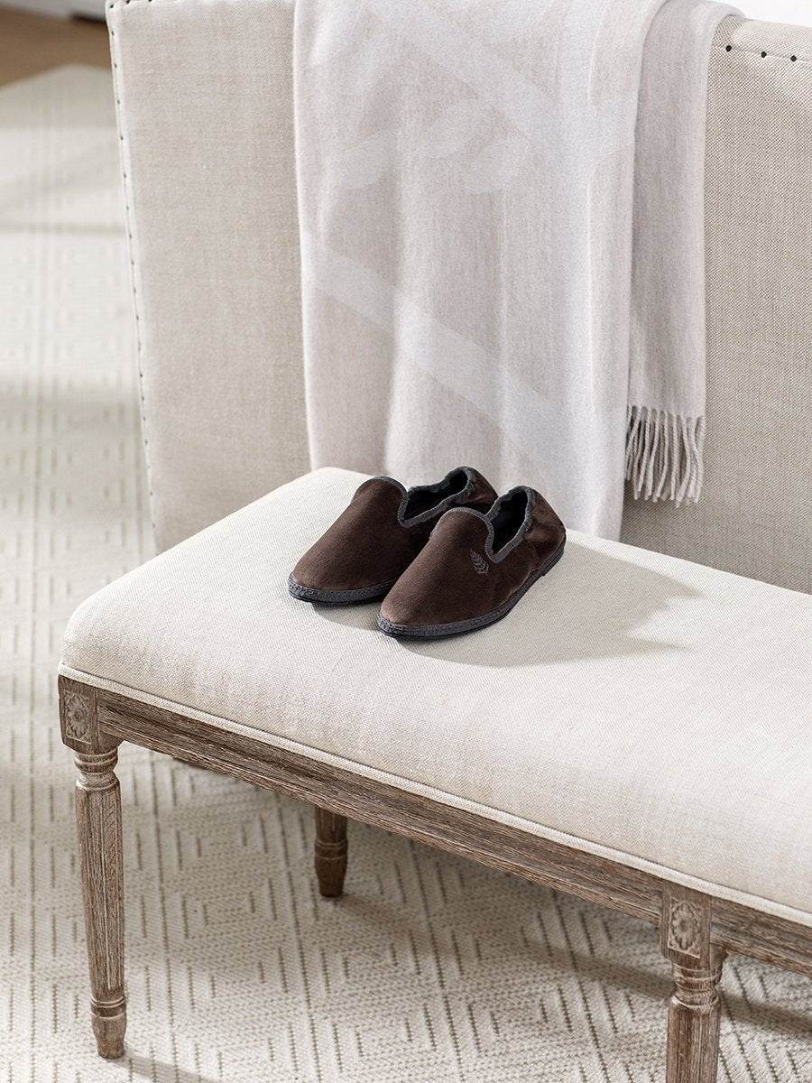 Four Seasons Velvet Slippers in Hampshire Charcoal placed on a bench in a cozy living room setting