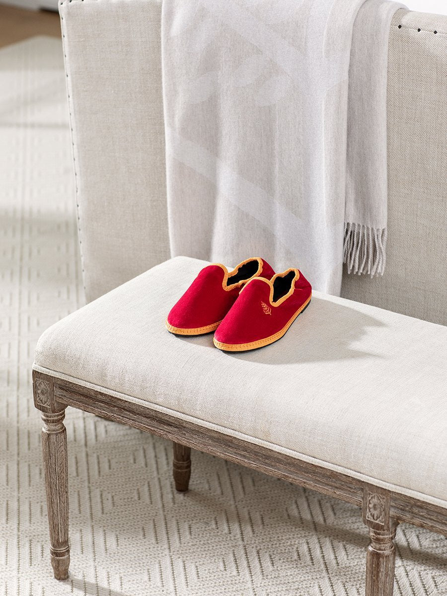 Four Seasons Velvet Slippers in Miami Rose placed on a bench in a cozy living room setting
