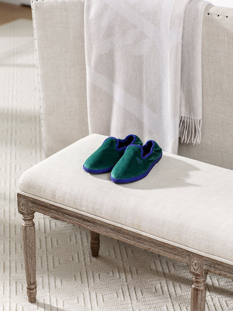 Four Seasons Velvet Slippers in Anguilla Green placed on a bench in a cozy living room setting