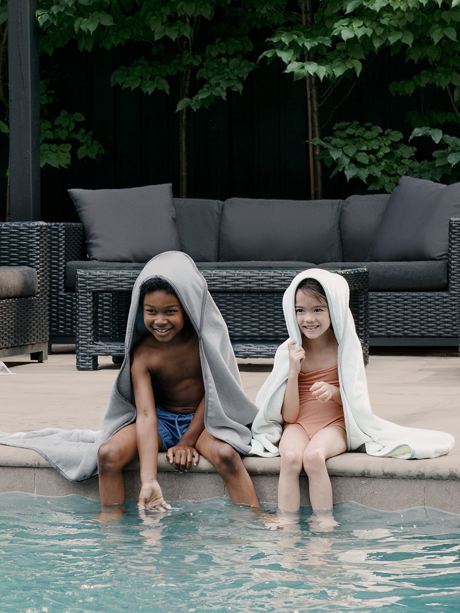 Two children splashing in a pool, each wearing a hooded towel.
