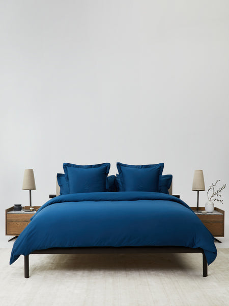 A bed covered with a Rivera Navy-colored duvet and several pillows delicately stacked.