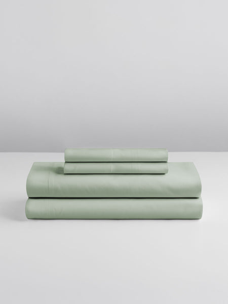 A set of Florentine Sage-colored sheets, folded into perfect rectangles and stacked on a flat surface.