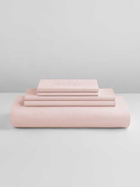 A set of Kyoto Blush-colored sheets, folded into perfect rectangles and stacked on a flat surface.