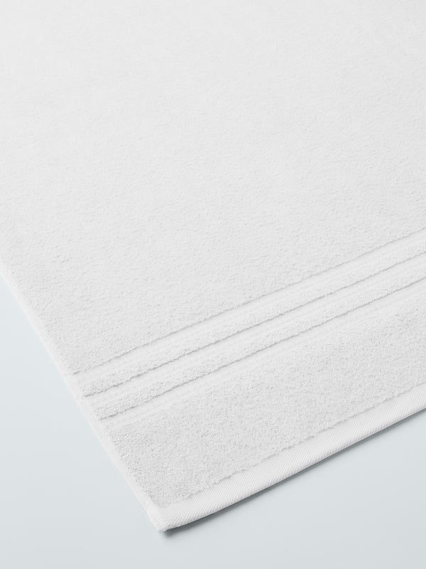 plush, folded bath sheets in a warm, inviting "Signature White" color. The towels have a thick, textured weave and subtle stripes