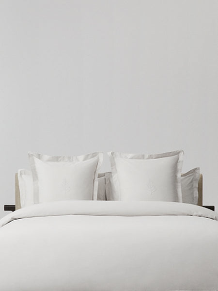 White pillows with decorative embroidery on a duvet, placed on top of a luxury bed.