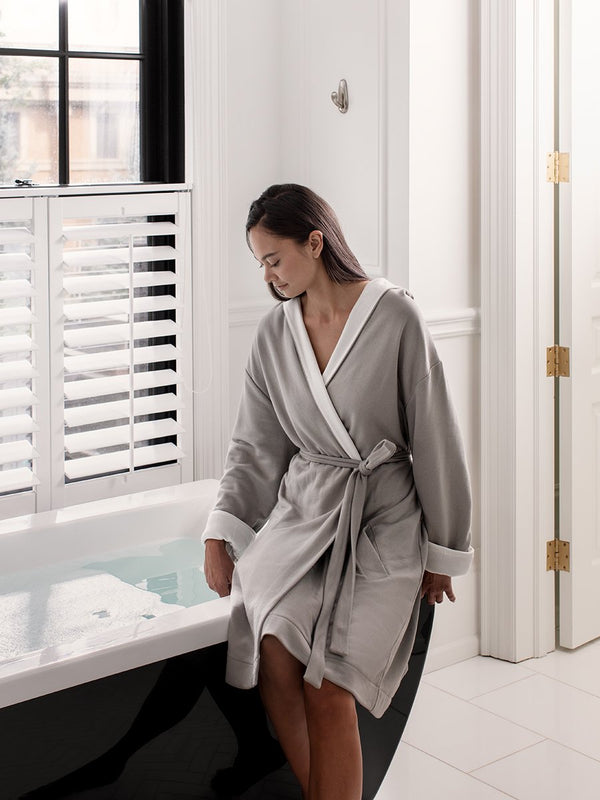 A woman dressed in a hooded robe. The exterior of the robe is a soft gray tone, while the interior features a contrasting white lining, giving it a sophisticated and clean look.