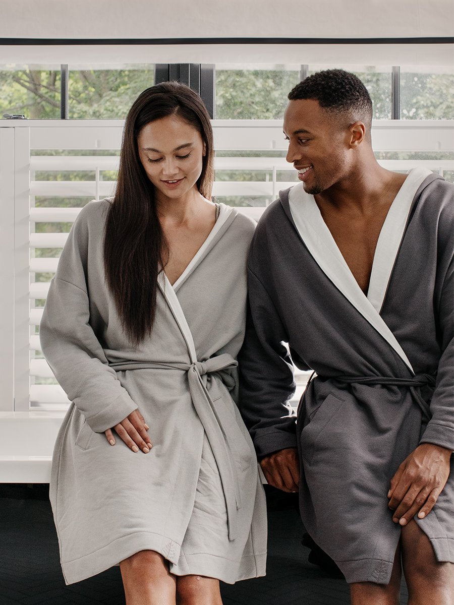 Two figures, a man and a woman, relaxing near a bathtub, dressed in white hooded robes.