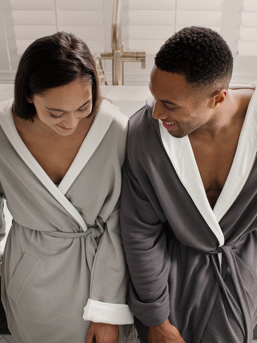 Two figures, a man and a woman, relaxing near a bathtub, dressed in white hooded robes.