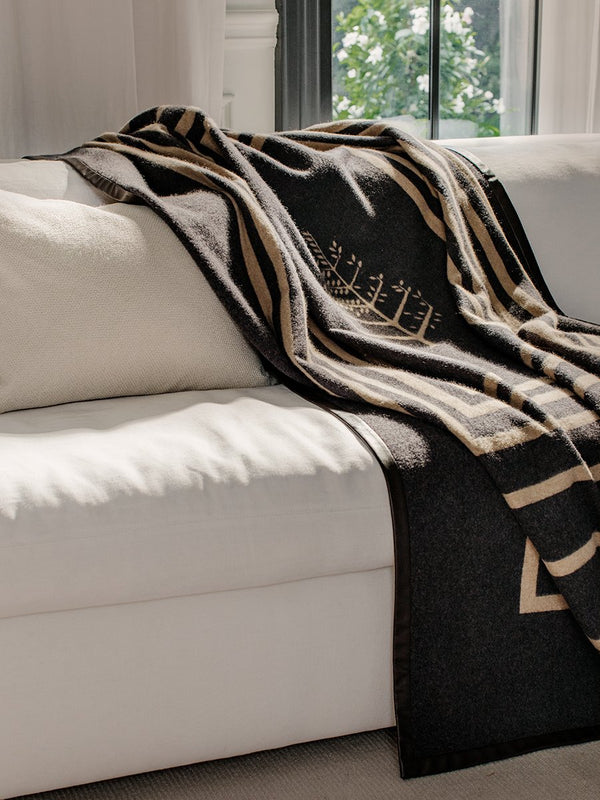 A black throw with a leather trim draped over a white sofa in a living room.