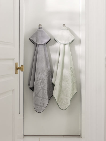 Two children's hooded towels, one in "Safari Sage" and one in "Mountain Grey", hanging on a door hook.