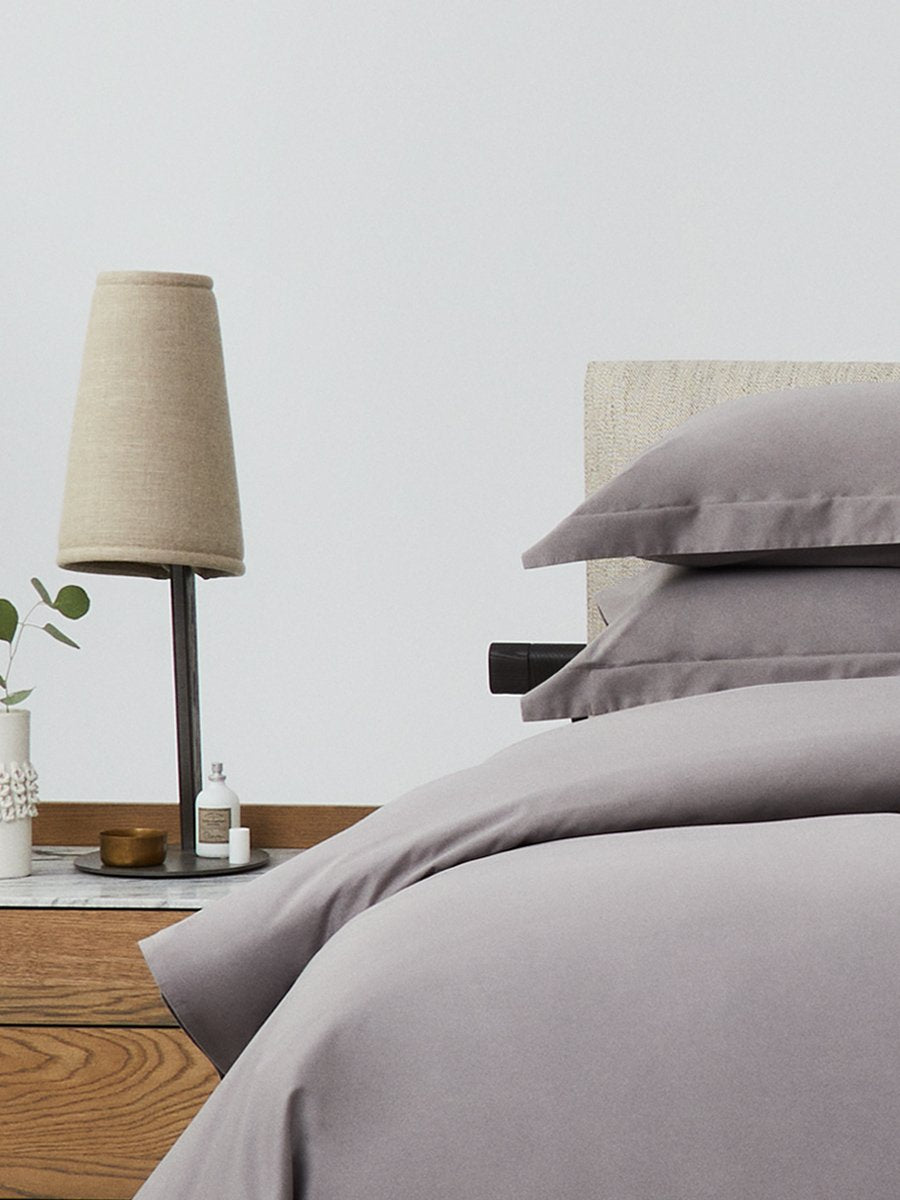 Bed dressed with a duvet in Hampshire Charcoal color and two pillows with embroidery along the edge.