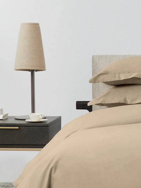 Bed dressed with a duvet in Egyptian Camel color and two pillows with embroidery along the edge.