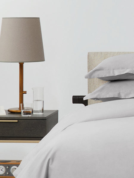 Bed dressed with a duvet in Turkish Silver color and two pillows with embroidery along the edge.