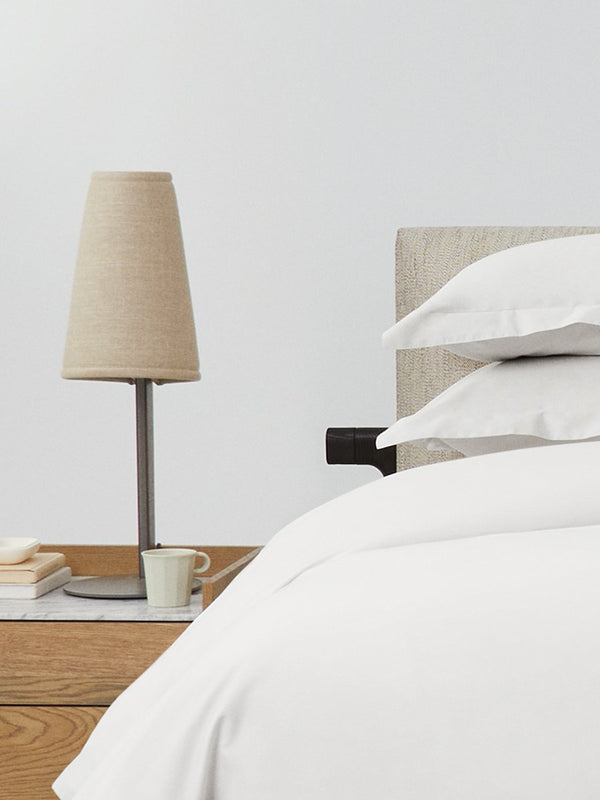 Bed dressed with a duvet in Signature White color and two pillows with embroidery along the edge.