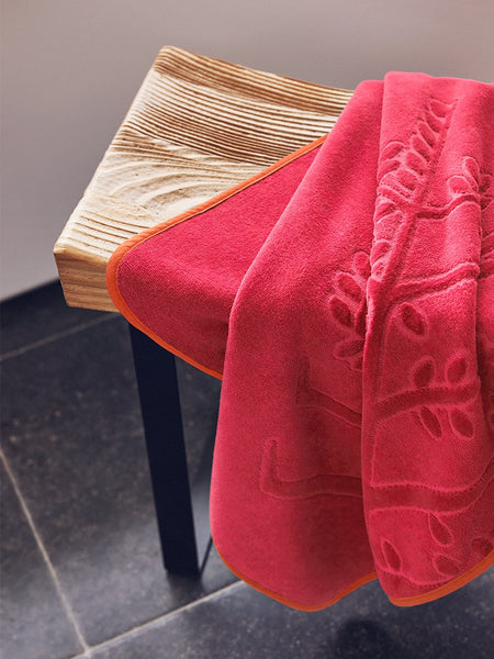 An "Coral Reef Pink" hooded towel folded on a wooden bench in a bathroom.